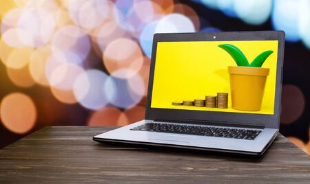 Laptop computer with money coin stack growing and tree shaped money box on yellow background on wooden table with blurred night light bokeh background, financial, business, saving money concept.の写真素材