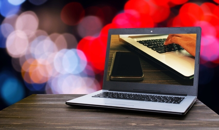 Laptop notebook computer with hand using laptop computer with smart phone on table with blur night light bokeh background, business working, online social media and searching data on website conceptの写真素材