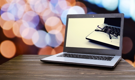 Laptop computer with Laptop computer with eyeglasses in screen on wood table with blurred night light bokeh background, selective focus, vintage tone, technology business, online social media conceptの写真素材