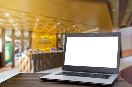 Laptop computer with white blank screen on wooden table with blurred indoor lobby at hotel background, selective focus, copy space, working outside office, online social media, searching data conceptの写真素材