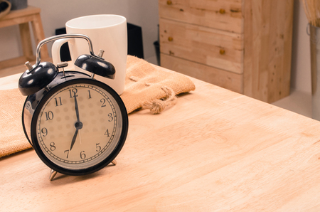 white coffee cup and black retro alarm clock times at 7 o'clock morning on wooden table, selective focus, copy space, vintage color toneの写真素材
