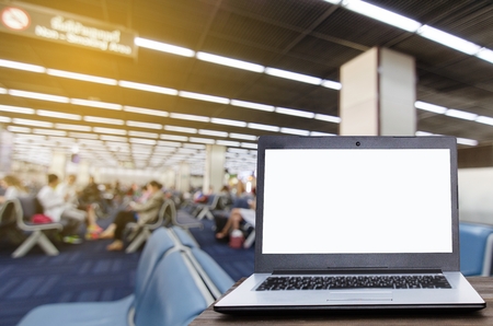 Laptop computer with white blank screen on wooden table with blurred in airport terminal waiting room, selective focus, copy space, working outside office, online social media, searching data conceptの写真素材