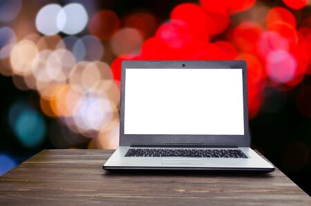 Laptop computer with white blank screen on wooden table with blurred night light bokeh background selective focus copy spaceの写真素材