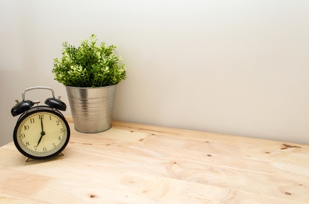 black vintage alarm clock times at 7 o'clock morning and green tree in silver pot small decorative on wooden table and white wall, vintage tone retro styleの写真素材