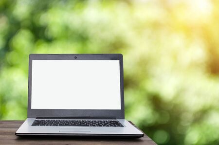 Laptop notebook computer with white blank screen on wooden table with nature green garden bokeh background with sunlight effect, business technology, online social media, searching data conceptの写真素材