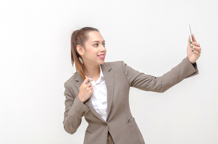 happy young asian business woman in suit beautiful smiling taking selfie with mobile phone or smartphone isolated on white background, social media technology and lifestyle conceptの写真素材