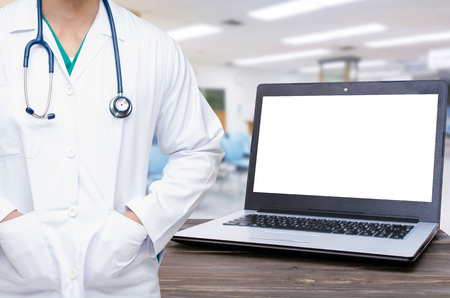 smart doctor with a stethoscope around his neck with laptop computer with white blank screen on wooden table with blurred view in hospital, heart health care and medical technology conceptの写真素材