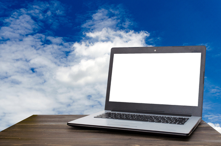Laptop computer with white blank screen on wooden table with blue sky and cloud background, selective focus, copy space, business working outside office, online social media, searching data conceptの写真素材