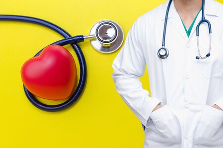 smart doctor with a stethoscope around his neck with red heart and a stethoscope on yellow background, heart health care and medical technology concept, selective focus.の写真素材