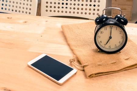 smartphone and black vintage retro alarm clock times at 7 o'clock morning on wooden desk in room,...