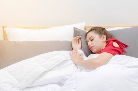 asian young woman in red pajamas sleeping on bed in bedroom with sunlight at the morning, soft focus, good morning, holiday, lifestyle conceptの写真素材