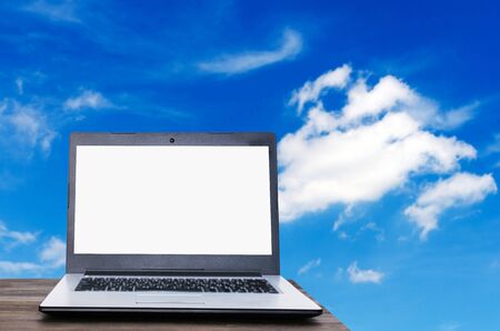 Laptop computer with white blank screen on wooden table with blue sky and cloud background, copy space, business working outside office, online social media, searching information conceptの写真素材