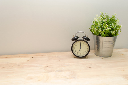 black vintage alarm clock times at 7 o'clock morning and green tree in silver pot small home decorative on wooden table and white wall, vintage tone retro styleの写真素材