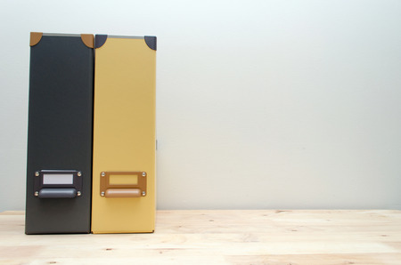 black and yellow office document file folders stack on wooden desk with white wall background, business conceptの写真素材