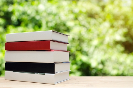 stack book on desk, no labels, blank spine with nature green garden bokeh background with sunlight effect, education back to school and business concept, color tone effect, copy spaceの写真素材