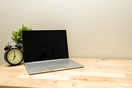Laptop notebook computer and black vintage retro alarm clock times at 7 o'clock morning on wooden table, workspace, selective focus, copy space, vintage color toneの写真素材