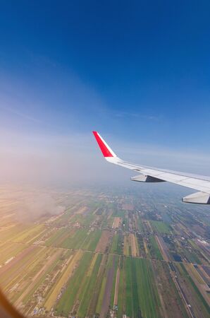 airplane wing flying in blue sky and cloud with view of earth from height from window, sunlight effect, travel and transport conceptの写真素材