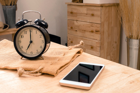 smartphone and black retro alarm clock times at 7 o'clock morning on wooden table, selective focus, vintage color toneの写真素材