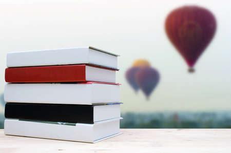 stack book on desk, no labels, blank spine with blurred view of hot air balloon in the sky background, education back to school, landscape nature and business concept, selective focus, copy spaceの写真素材