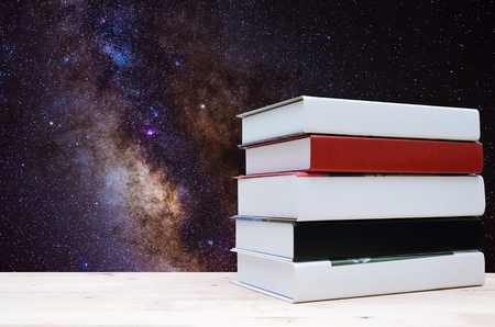 stack book on desk, no labels, blank spine with milky way galaxy background, long exposure photograph, with grain or noise and soft focus. color tone effect, education back to school conceptの写真素材