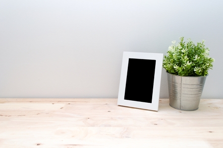blank black frame mock up white picture frame with mini leaf green plant tree in silver pot small home decorative on wooden desk with white wall background, home decoration concept, copy spaceの写真素材