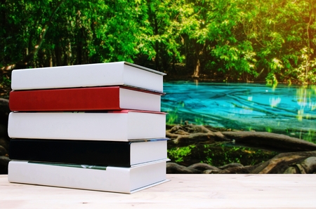 stack book on desk, no labels, blank spine with blurred view of amazing beautiful emerald pool and blue pool in forest with sunlight effectの写真素材