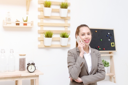 asian young business woman beautiful smile standing and talking on mobile smartphone in office, social network technology, business lifestyle and working woman concept, soft focusの写真素材