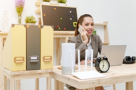 asian young business woman beautiful smile talking smartphone on wooden desk with laptop computer, soft focus, sunlight effect, social network technology, business lifestyle and working woman conceptの写真素材