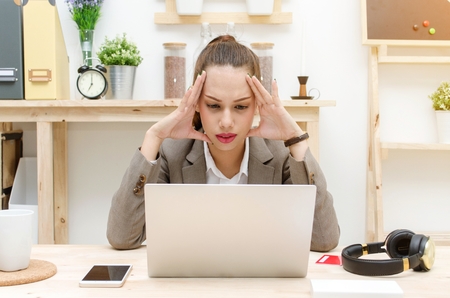stressed asian young business woman working on laptop computer on wooden desk at office, tired bored overworked, social network technology, business lifestyle and working woman concept, soft focusの写真素材