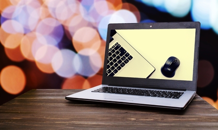 Laptop computer with Laptop computer with wireless mouse in screen on wooden desk with blurred night light bokeh background, selective focus, vintage tone, technology business conceptの写真素材