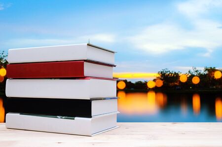 stack book on desk, no labels, blank spine with blurred view of twilight public park and botanical garden,blurred Photo with bokeh and reflection on water, education back to school, nature conceptの写真素材