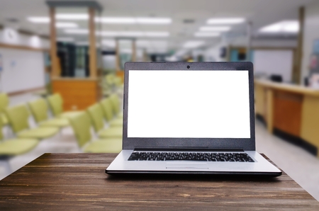 Laptop notebook computer with white blank screen on wooden desk with blurred view of empty chairs in clinic or hospital, heart health care and medical technology concept, selective focus, copy spaceの写真素材