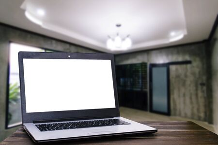 laptop computer with white blank screen for presentation on wooden desk with blurred view of modern living room interior at home, copy space, working at home, online social media, searching conceptの写真素材
