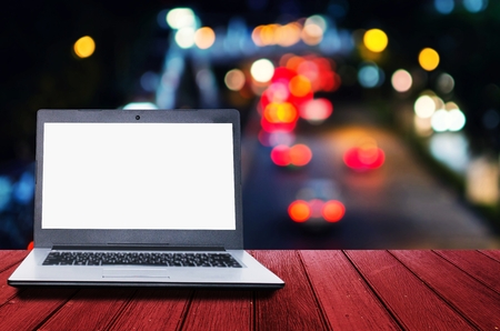 Laptop computer with white blank screen for presentation on wooden desk with abstract night light bokeh, blurred view of street traffic light in the city, copy space, business technology conceptの写真素材