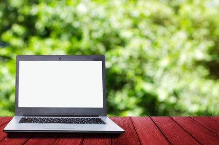 Laptop computer with white blank screen for presentation on wooden desk with abstract blurred nature green bokeh with sunlight for background, copy space, business technology conceptの写真素材