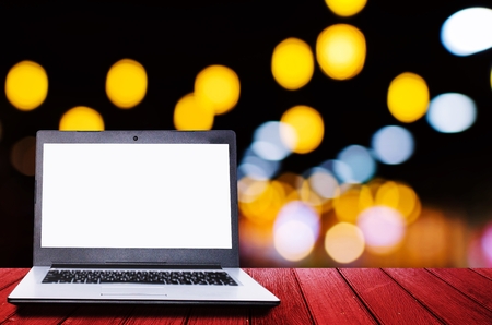 white blank screen laptop computer on wooden desk for presentation with blurred image of abstract night light bokeh on dark background, copy space, technology conceptの写真素材