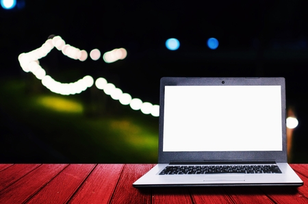 white blank screen laptop computer on wooden desk for presentation with blurred image of night light bokeh of night festival in garden background, copy space, technology conceptの写真素材