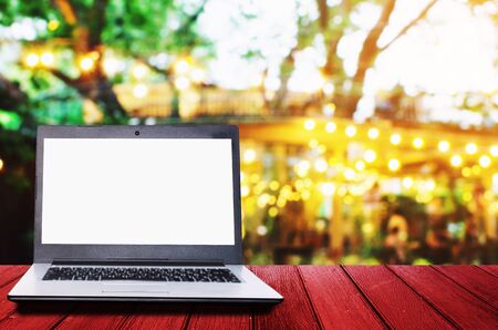 white blank screen laptop computer on wooden desk for presentation with blurred image of abstract night light bokeh of night festival in garden background, copy space, technology lifestyle conceptの写真素材