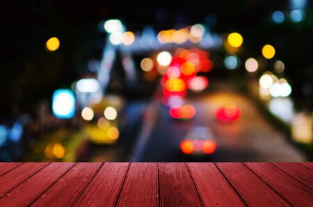 empty wooden red floor, desk or terrace copy space for display of product or object presentation with abstract blurred image of light bokeh view of street traffic light in the city at nightの写真素材