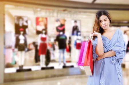 cheerful asian young woman holding shopping bags while standing at the clothing store in department store shopping mall, online payment, shopping online, lifestyle technology conceptの写真素材