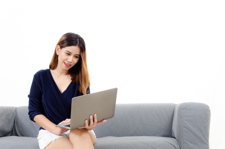 happy beautiful young asian woman using laptop computer on on sofa at home on white background, soft focus, lifestyle smart communication technology, online shopping and payment online conceptの写真素材