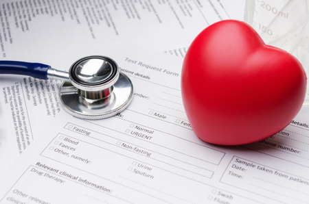 close up stethoscope, red heart, beaker and patient information form on desk, heart healthcare technology, medical diagnosis, medical report record and history patient concept, selective focusの写真素材