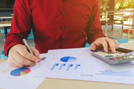 young accountant or business man using claculator and hand writing working finances and calculate with chart report on desk, home office, plan money cost saving, business, economy conceptの写真素材