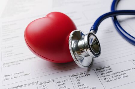 close up stethoscope, red heart and patient information form on desk, heart attack, heart disease, medical diagnosis, medical report record and history patient concept, selective and soft focusの写真素材