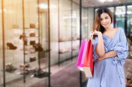 cheerful young asian woman holding shopping bags while standing at trendy shoes shop in department store shopping mall, online payment, shopping online, lifestyle technology conceptの写真素材