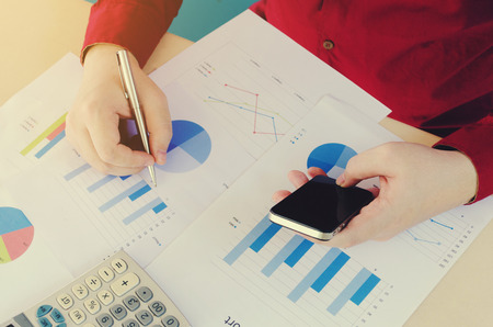 man using smart phone and hand writing working finances and calculate with chart report on desk, home office, plan money cost savings, business, economy conceptの写真素材