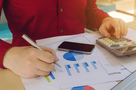 young man calculate using calculator with income and expenses chart report on desk at home office, plan money cost saving, business technology and economy concept, selective focus, vintage color toneの写真素材