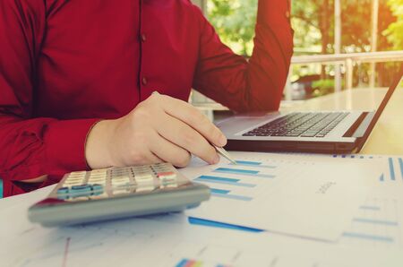 young man stress and calculate using calculator with laptop computer, income and expenses chart report on desk at home office, plan money cost savings, business technology and economy conceptの写真素材