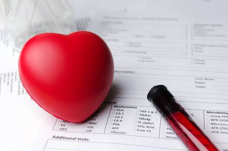 red heart, test tube, beaker and patient information form on desk, heart healthcare technology, medical diagnosis, blood test, medical report record and history patient concept, selective focusの写真素材
