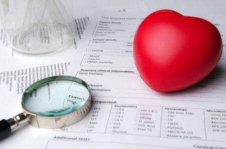 red heart, magnifying glass, test tube, beaker and patient information form on desk, heart healthcare technology, medical diagnosis, heart disease, medical report record and history patient conceptの写真素材